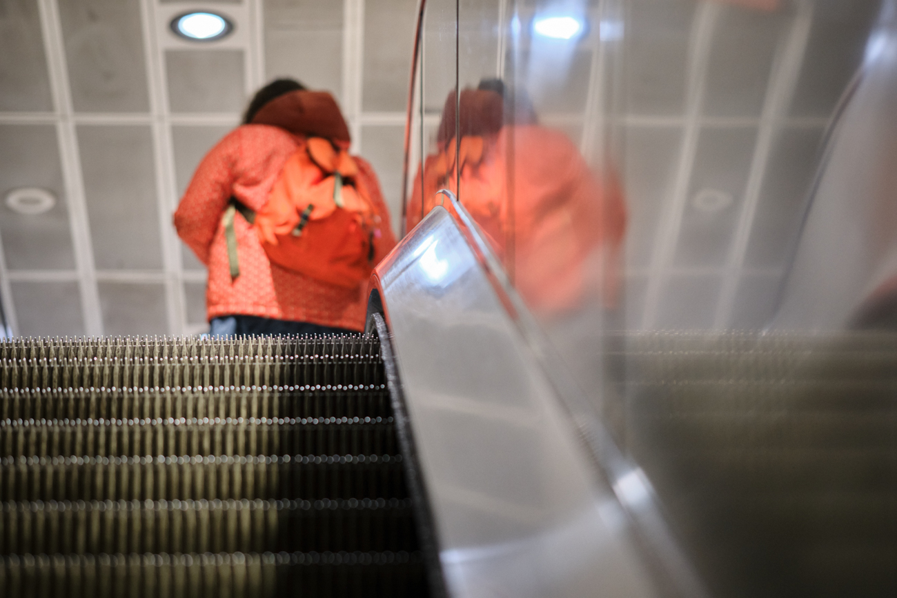 Close-up perspective of escalator treads with a blurred figure in a red jacket reflected in polished metal.