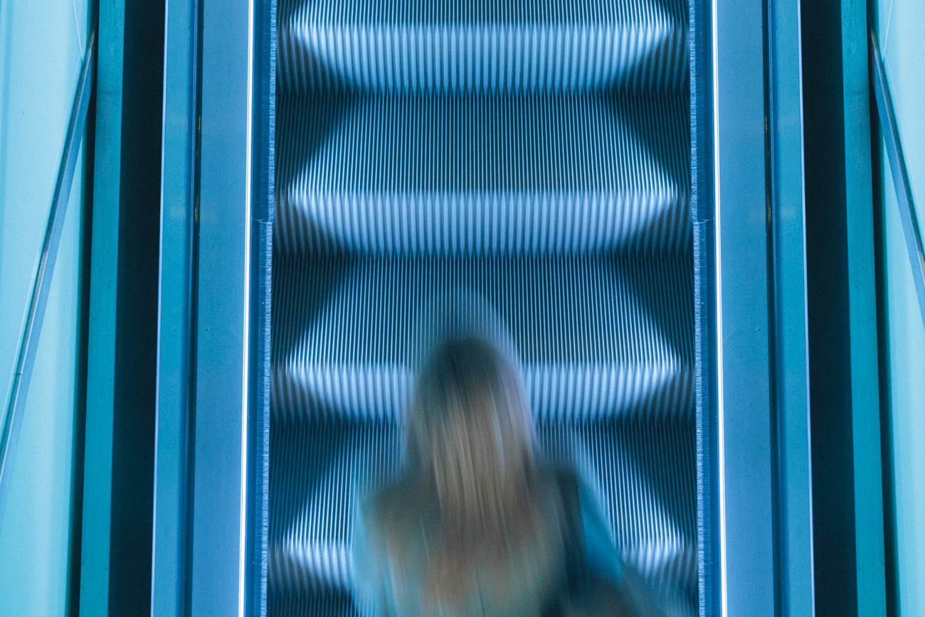 Motion blurred silhouette of a person on an escalator with glowing blue neon geometric lines.