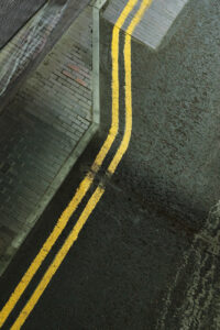 Abstract top-down view of wet asphalt, yellow road lines, and brick sidewalk textures.