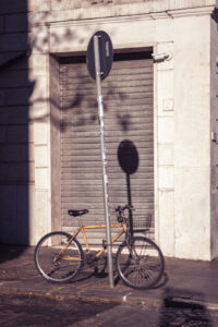 A yellow bicycle leaning against a pole in front of a closed industrial shutter in warm light.