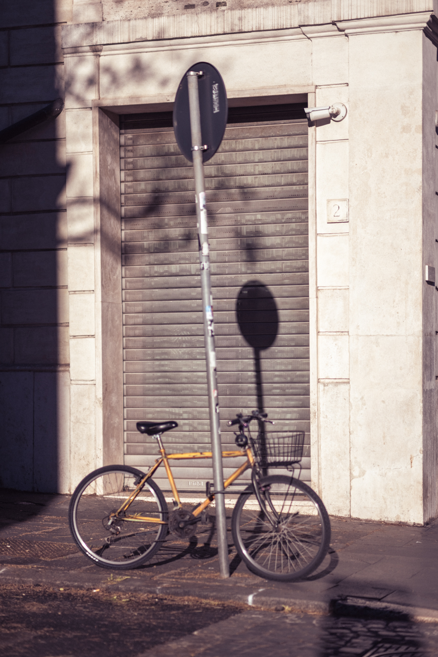 A yellow bicycle leaning against a pole in front of a closed industrial shutter in warm light.