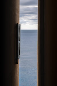 Minimalist view of the sea horizon through a narrow vertical architectural opening with a shutter.