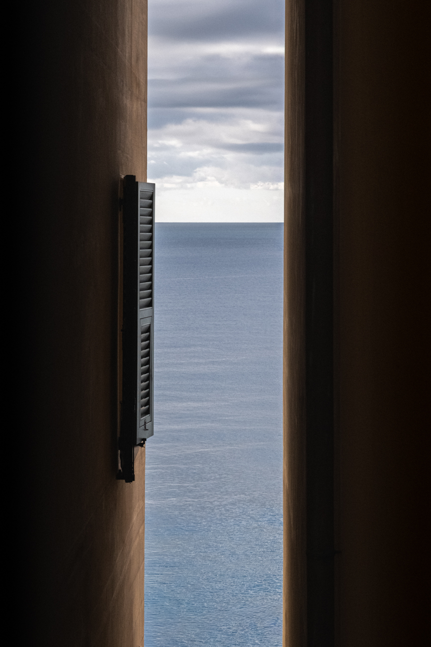 Minimalist view of the sea horizon through a narrow vertical architectural opening with a shutter.