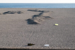 Fine art landscape of a pebble beach with discarded glass and plastic bottles, exploring human impact.