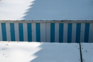 Graphic study of blue and white vertical stripes on a structure framed by white planes and shadows.