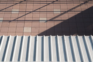 Architectural composition of a white corrugated roof and pink floor tiles with geometric shadows.