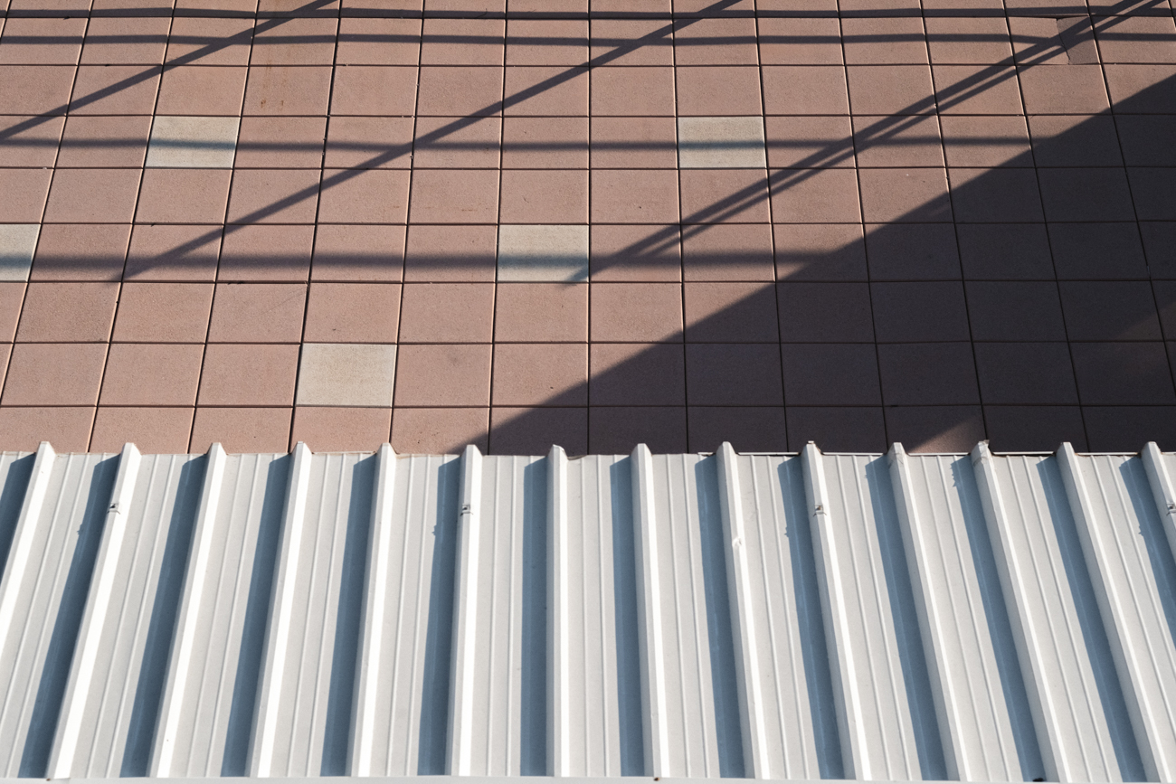 Architectural composition of a white corrugated roof and pink floor tiles with geometric shadows.