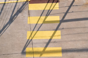 Top-down view of concrete with yellow rectangular markings and linear shadows from overhead structures.